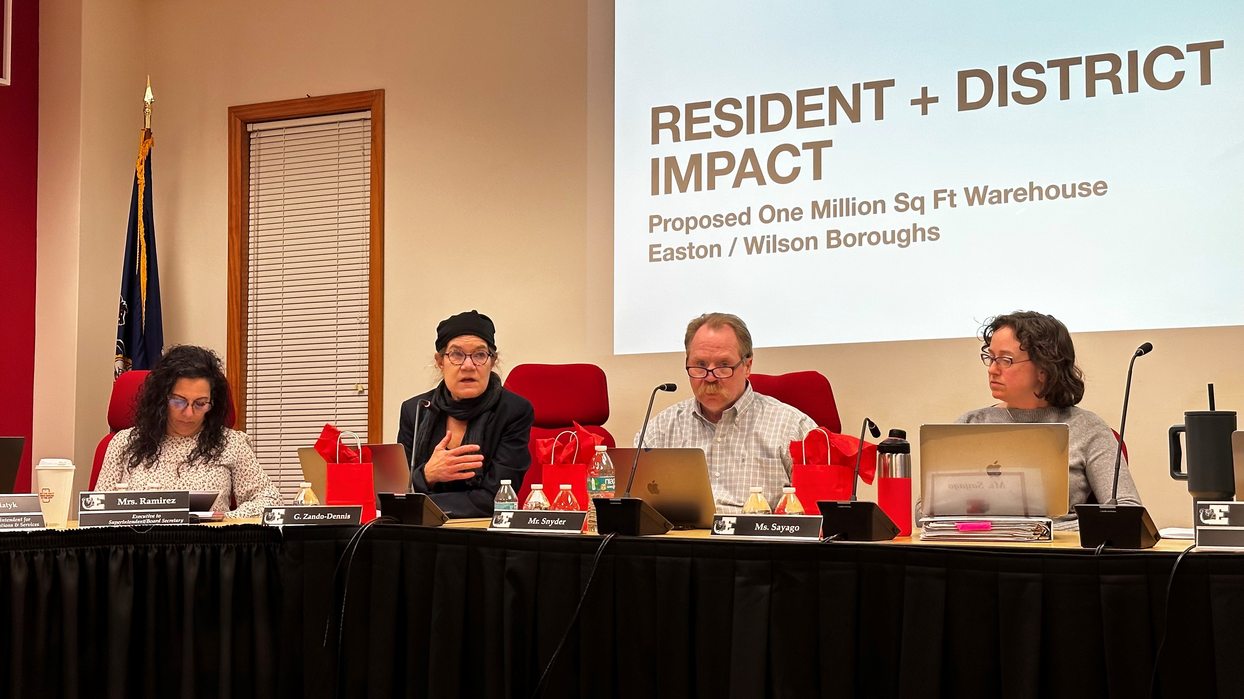 A panel of four people each sitting in a chair during a board meeting